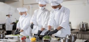 Chefs in face masks prepare takeaway food in professional kitchen